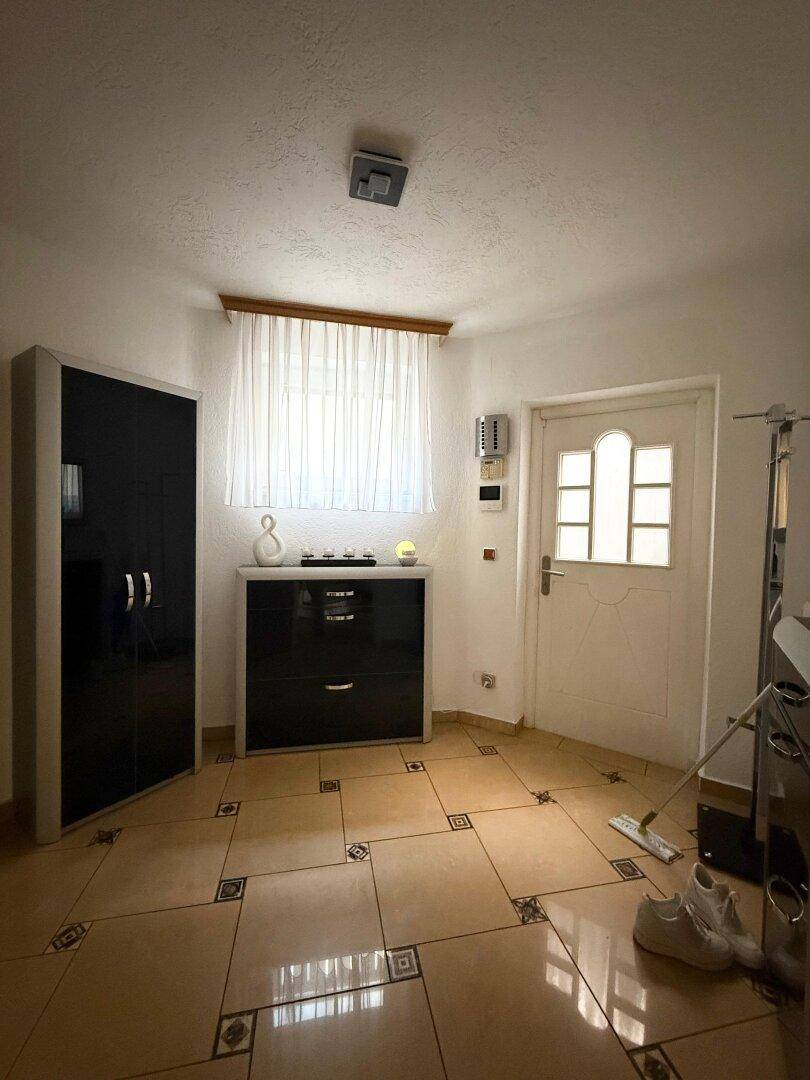 Eingangsbereich mit heller Tür, Fenster und dunklen Möbeln auf gemusterten Fliesen.