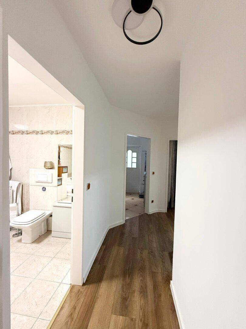 Heller Flur mit Laminatboden und Blick in ein angrenzendes Badezimmer.
