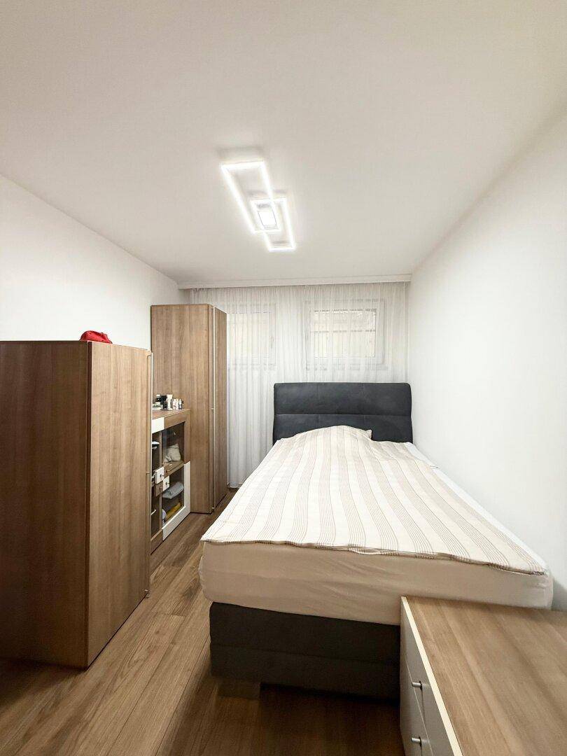 Gemütliches Schlafzimmer mit Holzboden, Einzelbett und Fenster mit Vorhängen.