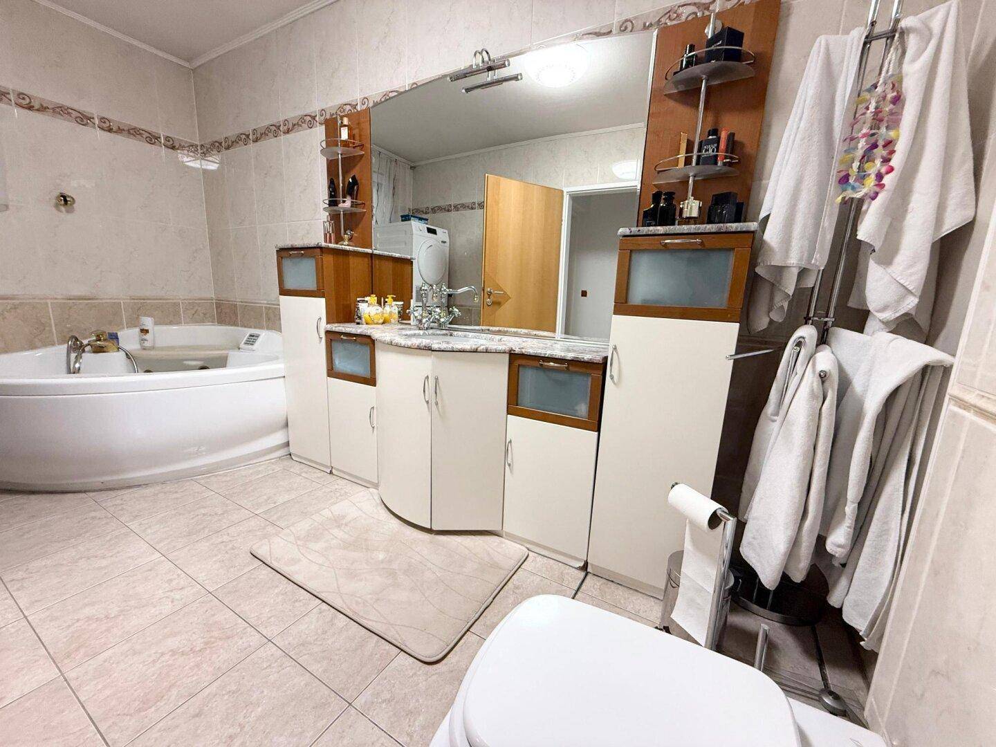 Helles Badezimmer mit Eckbadewanne, Doppelwaschbecken und großem Spiegel.