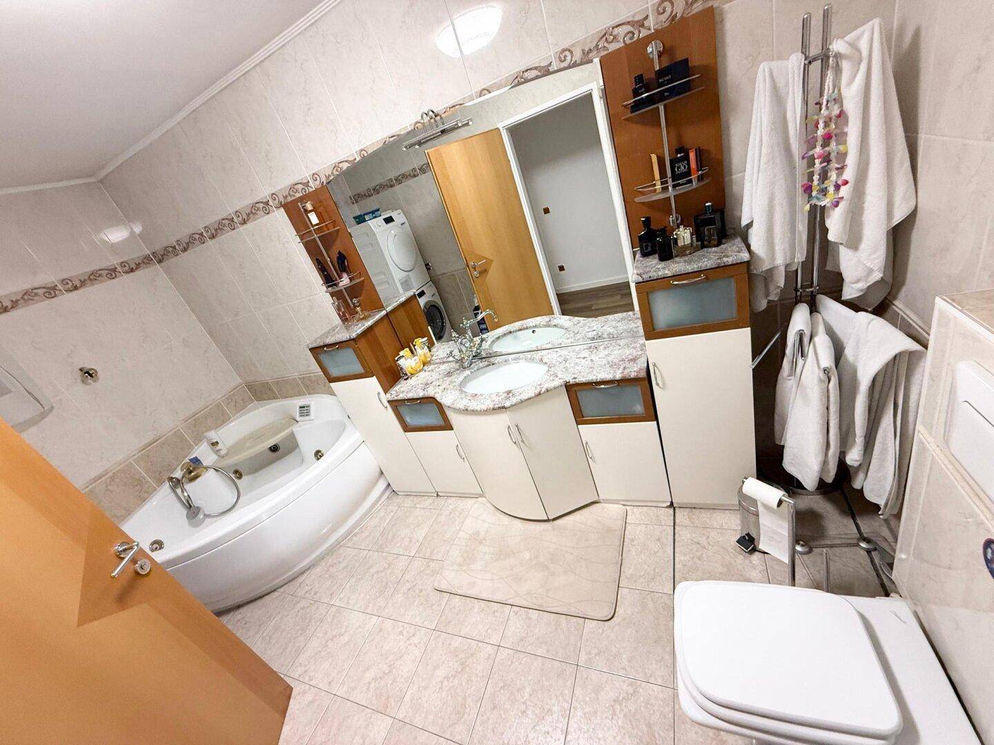 Geräumiges Badezimmer mit Eckbadewanne, Doppelwaschbecken und hellen Fliesen.