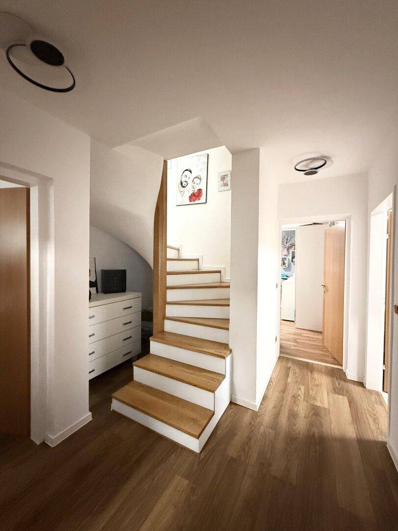 Heller Flur mit Holztreppe und Laminatboden, der die Etagen verbindet.