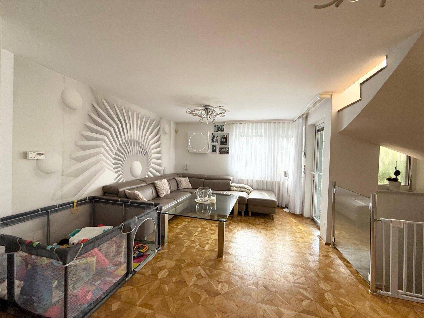 Geräumiges Wohnzimmer mit Ecksofa, Parkettboden und Zugang zur Treppe.