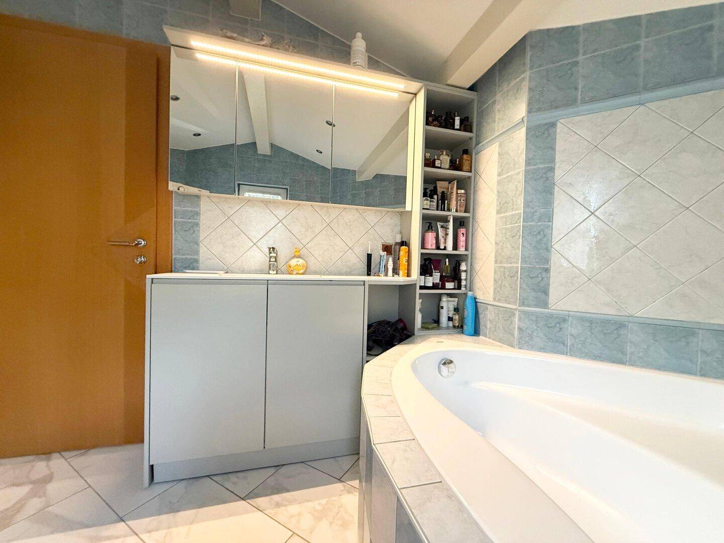Badezimmer mit Badewanne, Waschbecken und blauen Fliesen unter einer Dachschräge.