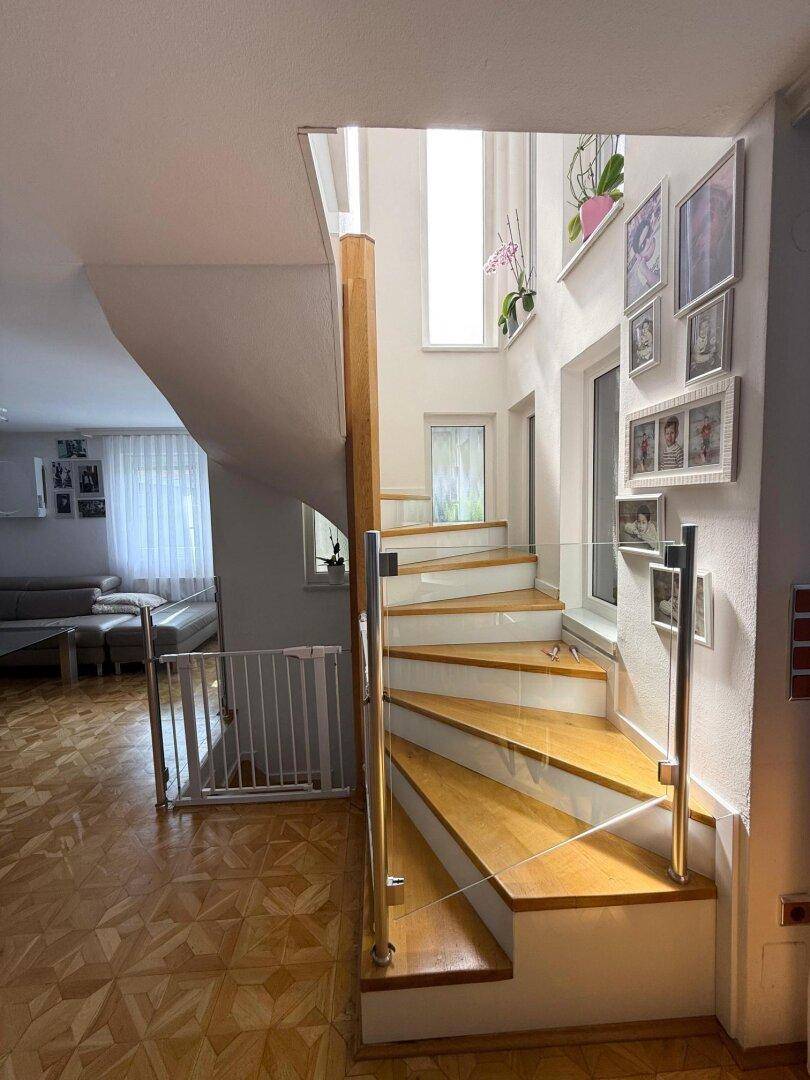 Helle Holztreppe mit Glasgeländer verbindet die Etagen in einem lichtdurchfluteten Bereich.