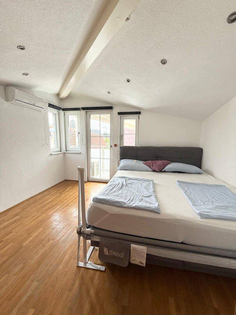 Helles Schlafzimmer im Dachgeschoss mit Holzboden, Klimaanlage und Zugang zum Balkon.