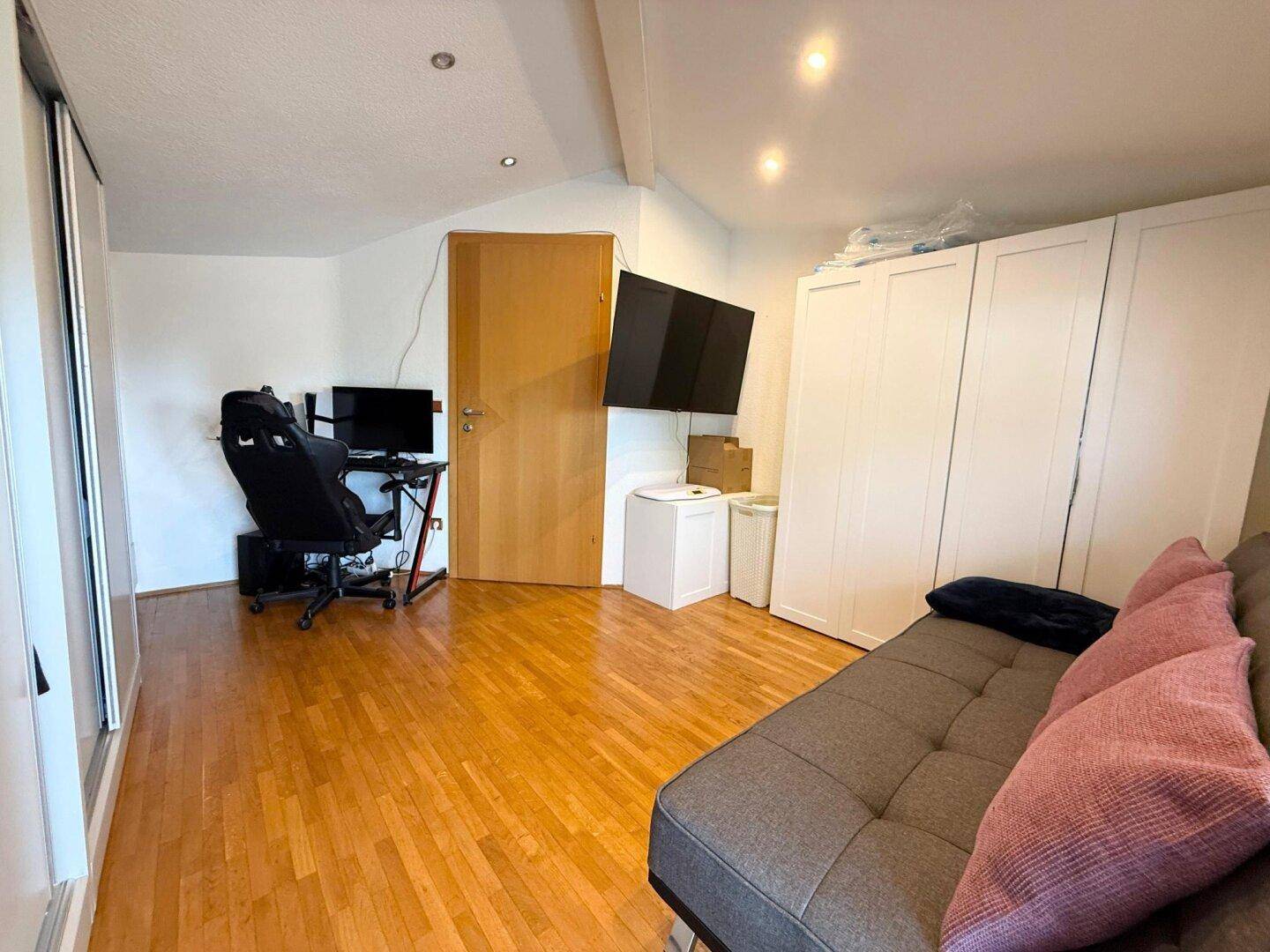 Vielseitiger Raum mit Holzboden, Sofa, Schreibtisch und praktischen Kleiderschränken.