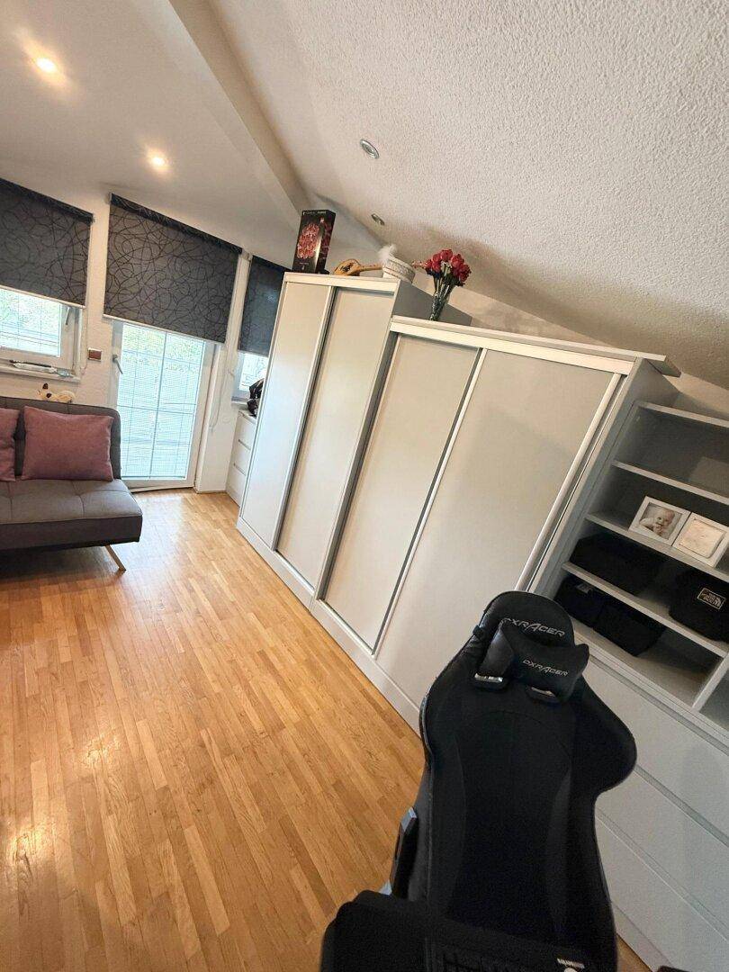 Dachgeschosszimmer mit Holzboden, Schränken und einem Sofa, ideal als Schlaf- oder Arbeitsbereich.