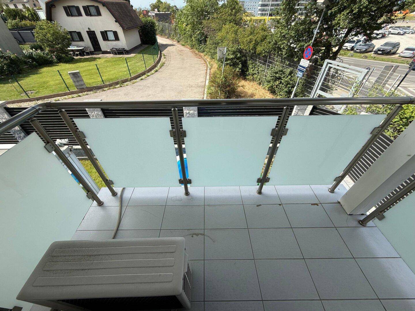 Balkon mit Fliesenboden und Glasgeländer, bietet Blick auf Grünflächen und die Umgebung.
