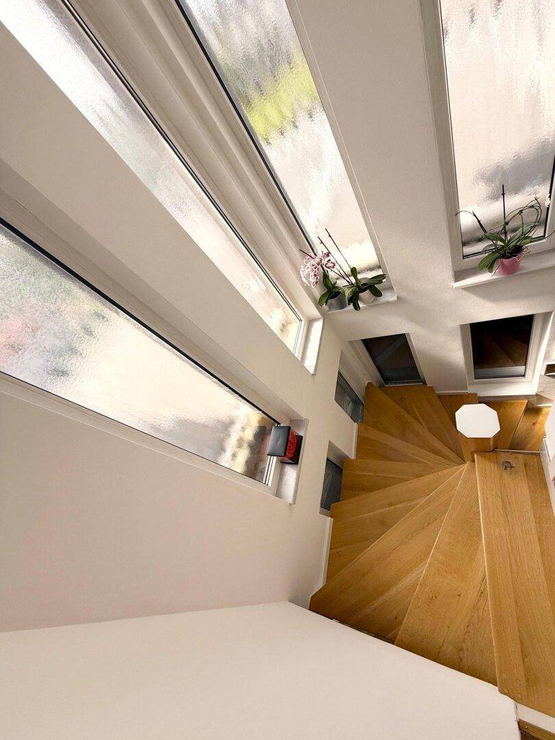 Helle Holzwendeltreppe mit großen Fenstern, die viel natürliches Licht hereinlassen.