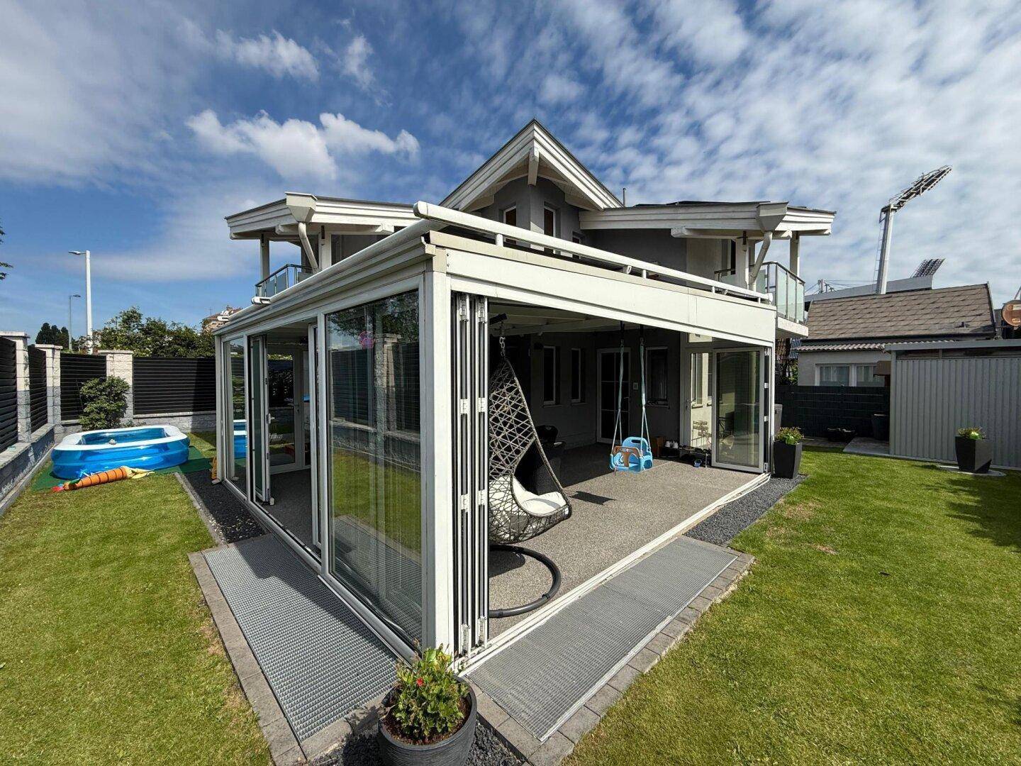 Haus mit großem Wintergarten, gepflegtem Rasen und kleinem Pool im Gartenbereich.
