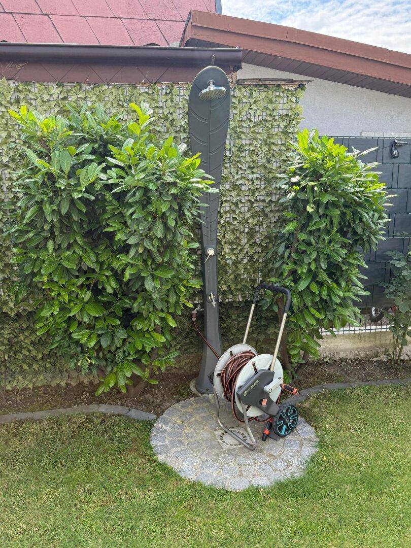Außendusche im Garten, umgeben von grünen Büschen, ideal für heiße Tage.