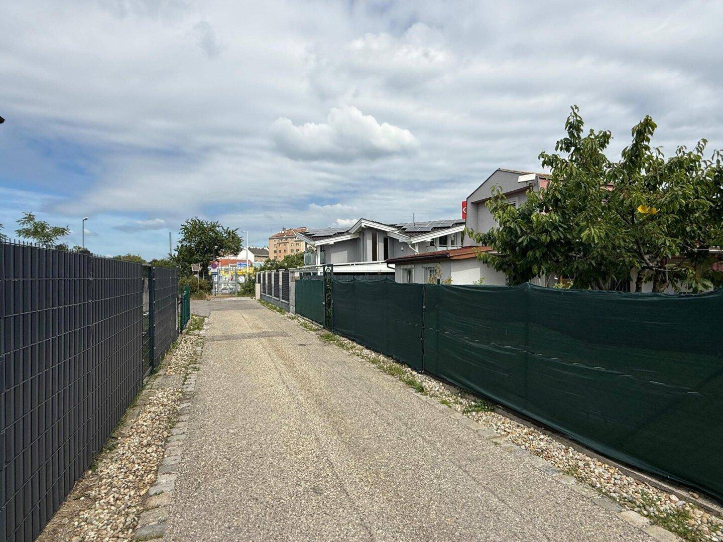 Zufahrtsweg zum Haus mit Zäunen auf beiden Seiten und Blick auf die Nachbarschaft.