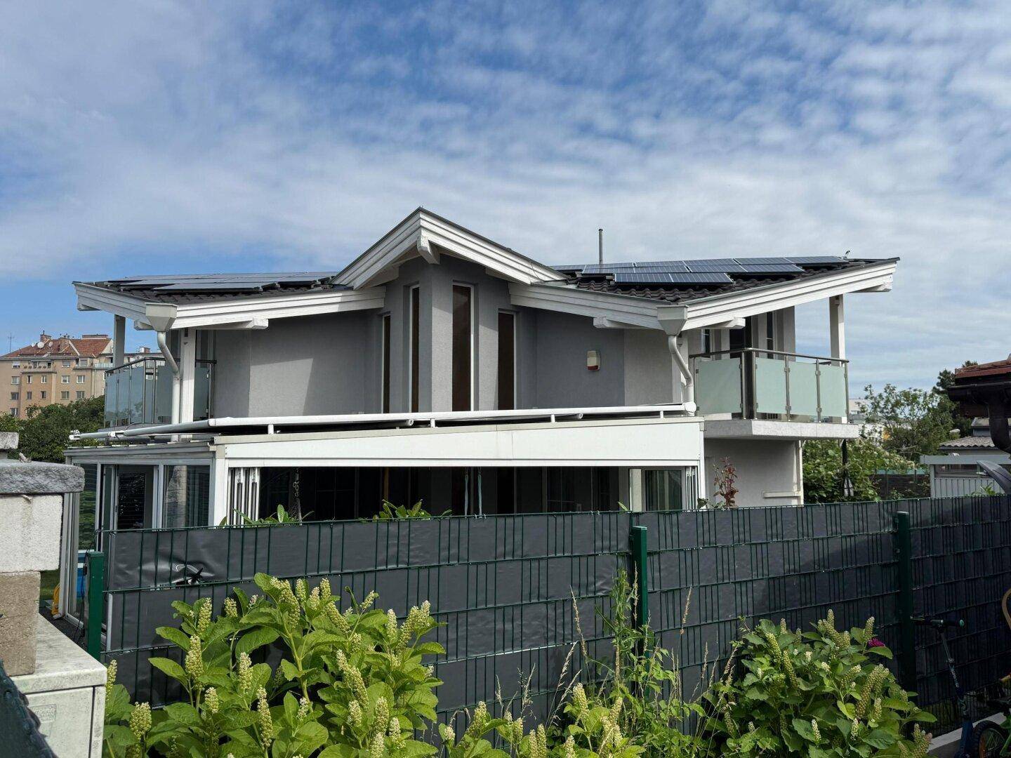 Modernes Haus mit Balkonen, Photovoltaikanlage auf dem Dach und ansprechender Architektur.