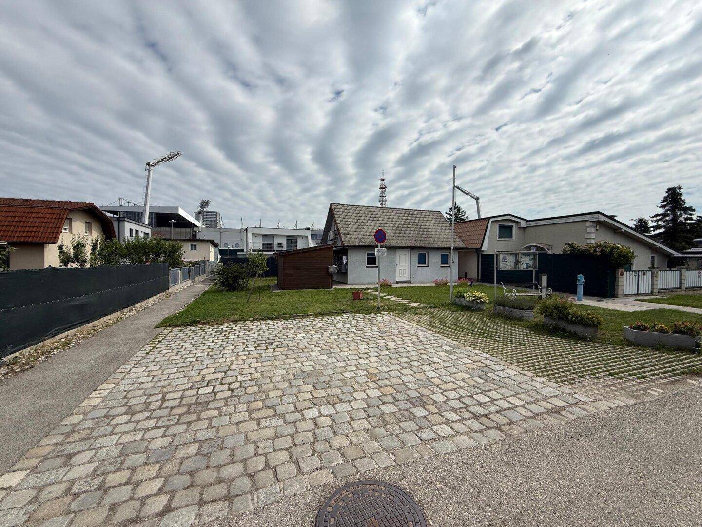 Außenparkplatz aus Kopfsteinpflaster mit Grünfläche und Blick auf die umliegenden Häuser.