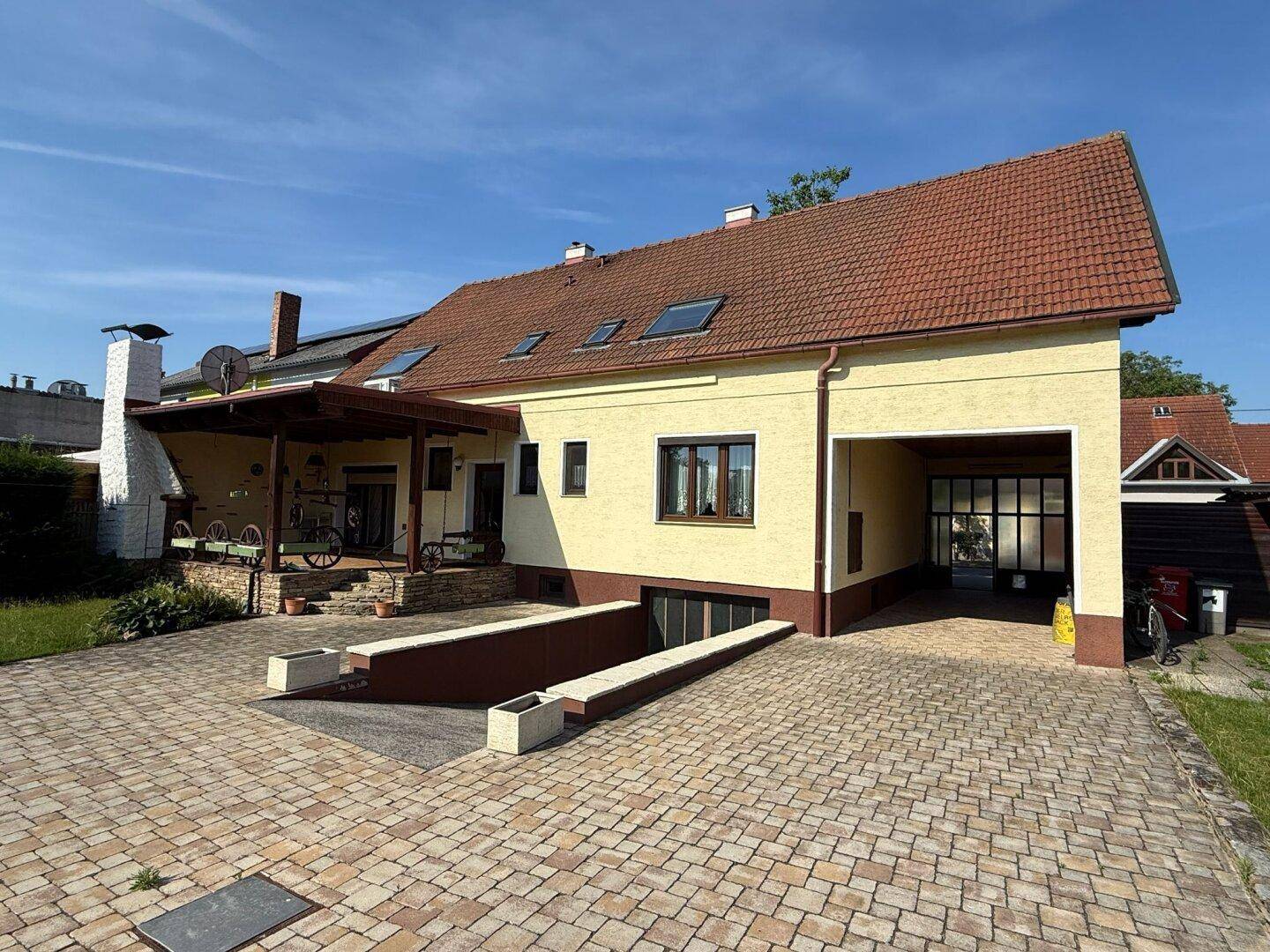 Hausfassade mit überdachter Terrasse, Einfahrt zur Tiefgarage und Carport.