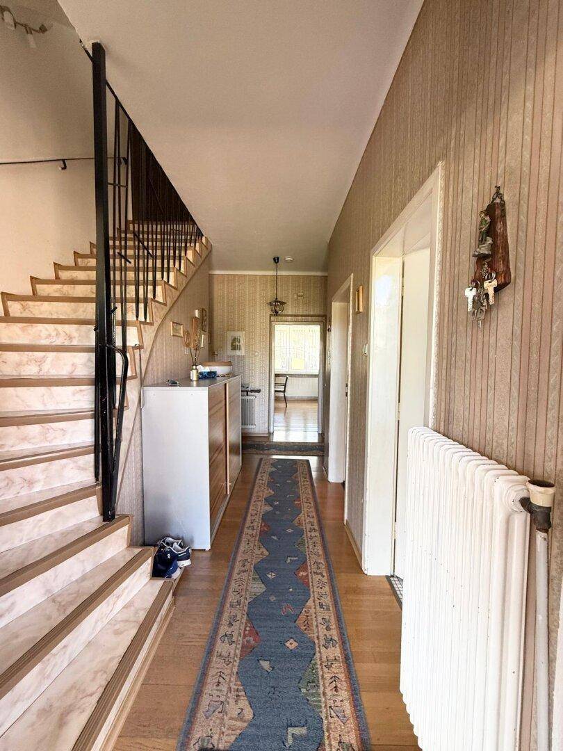 Heller Flur mit Marmortreppe, Holzfußboden und gemusterter Tapete.