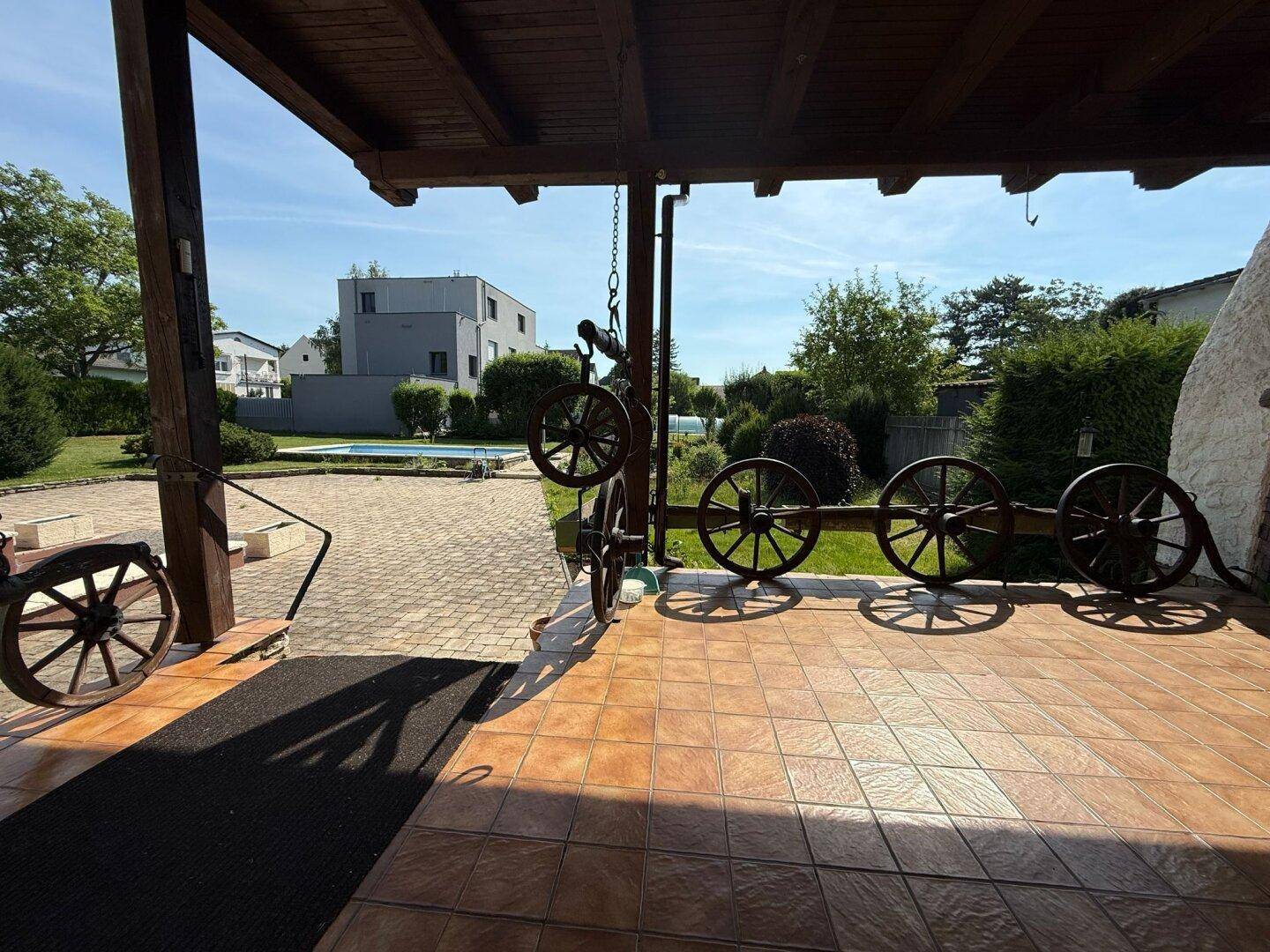 Überdachte Terrasse mit rustikalen Holzbalken und dekorativen Wagenrädern, Blick zum Pool.