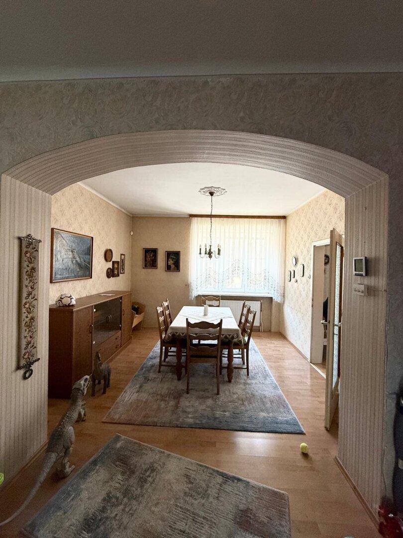 Geräumiges Esszimmer mit großem Holztisch, passenden Stühlen und gemusterter Tapete.