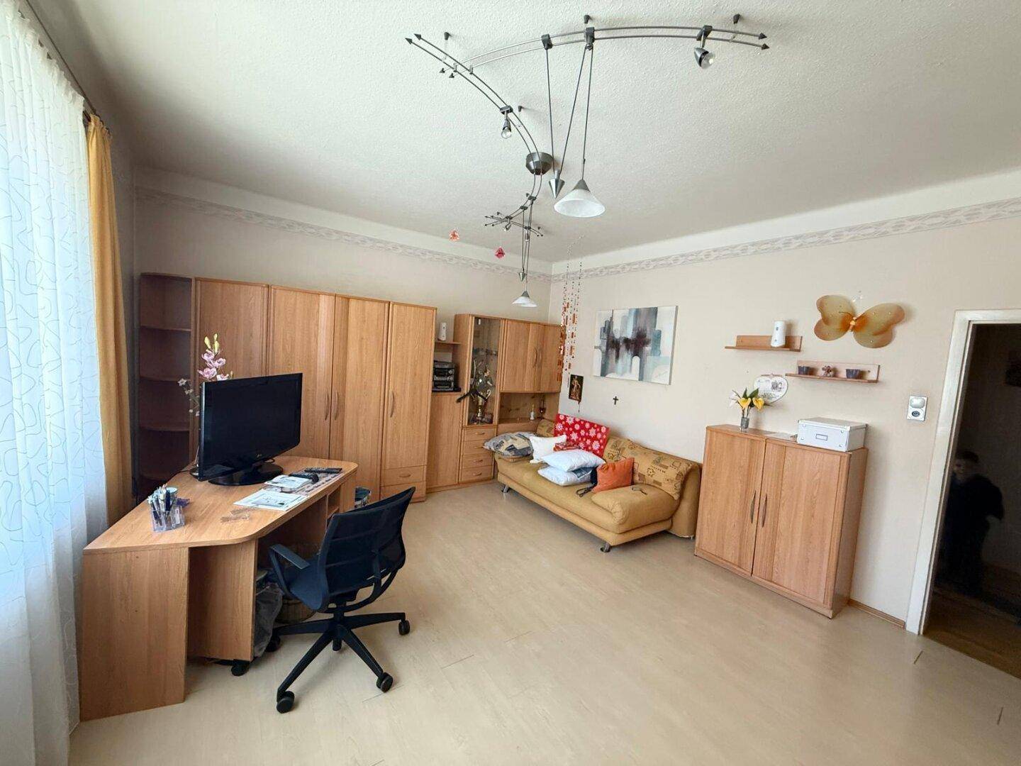 Helles Arbeitszimmer mit Schreibtisch, Holzmöbeln und einem kleinen Sofa.