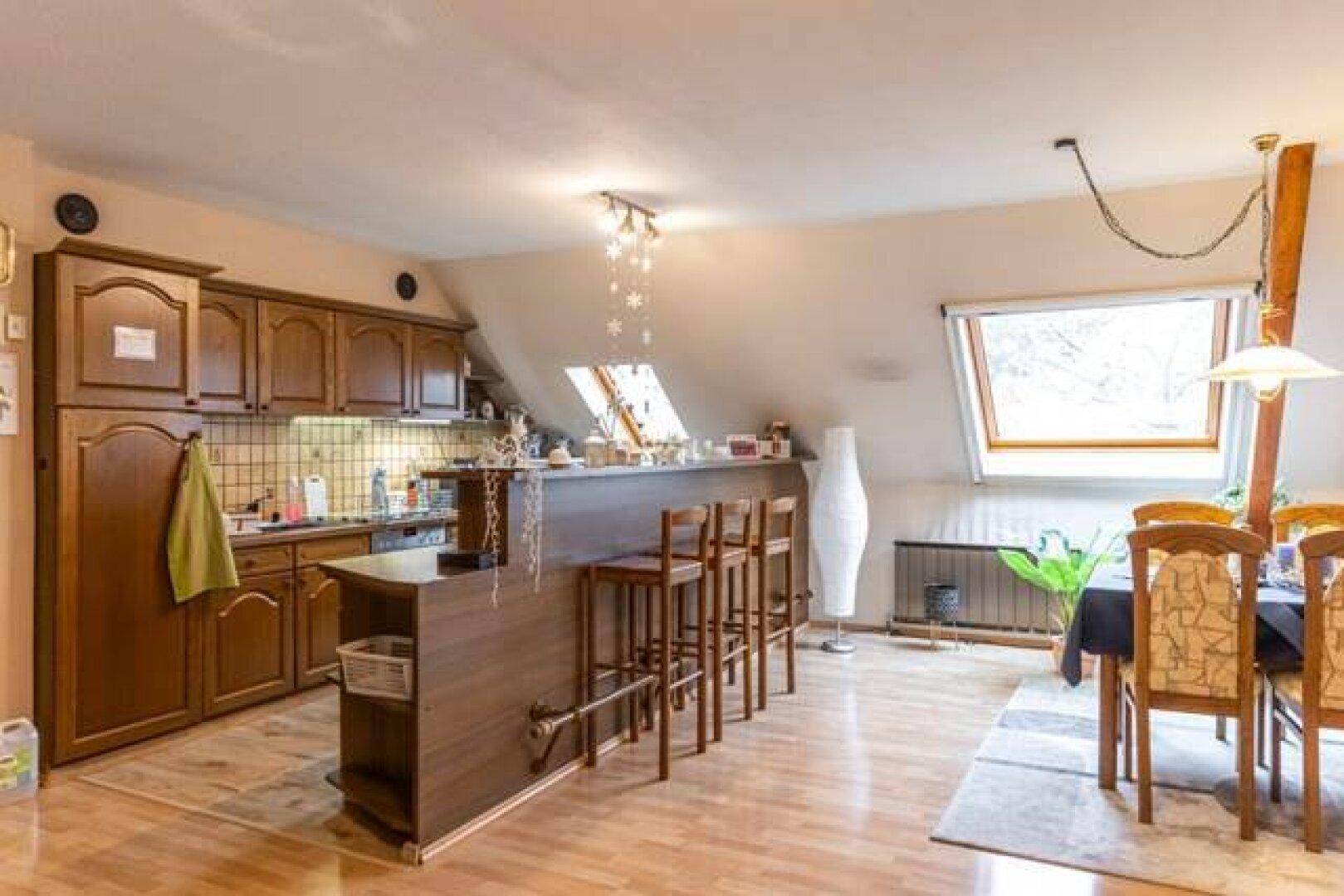 Küche in der Dachgeschosswohnung mit Holzschränken, Bar und Dachfenster.