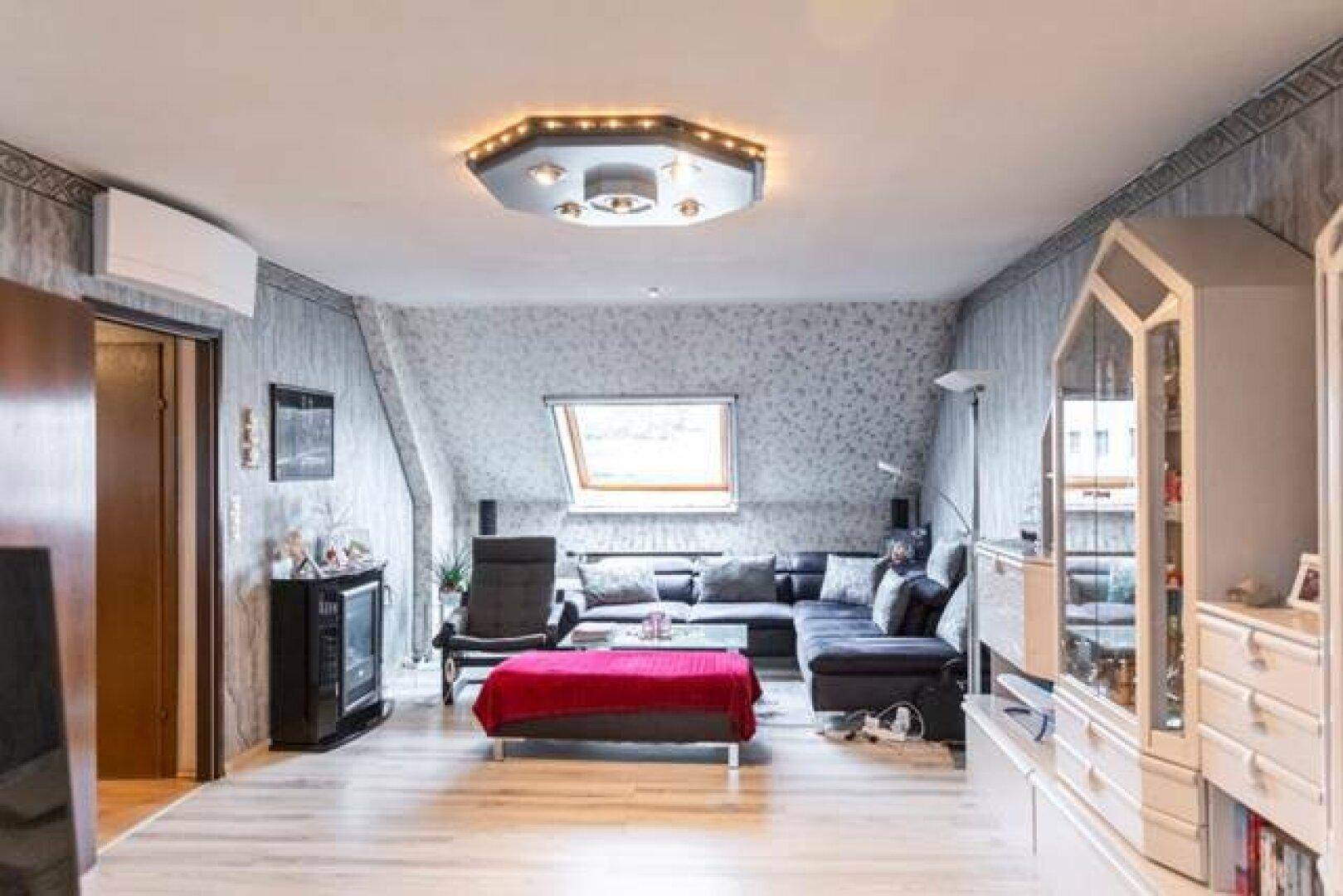 Gemütliches Wohnzimmer in der Dachgeschosswohnung mit Sofa, Fernseher und Klimaanlage.