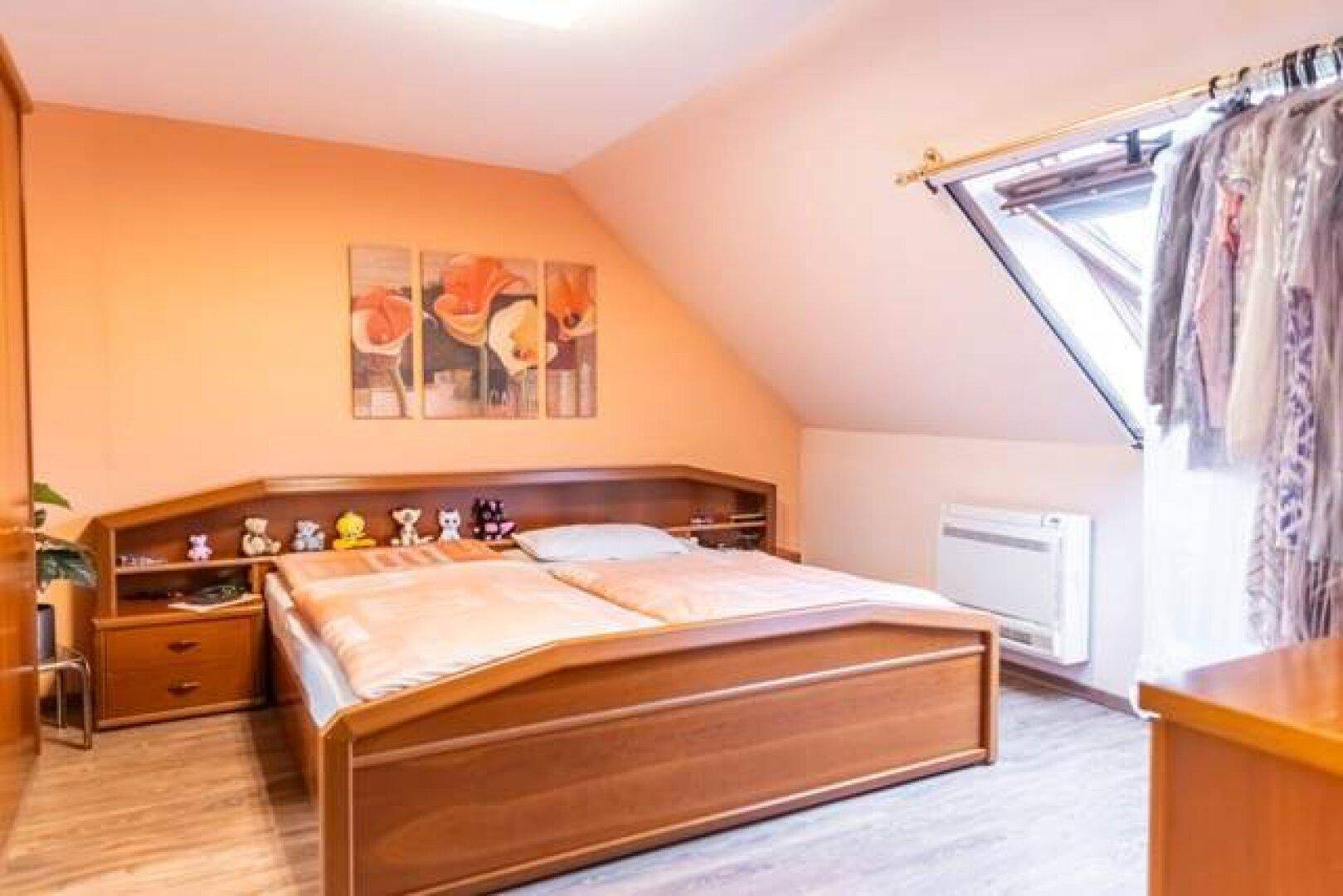 Schlafzimmer in der Dachgeschosswohnung mit orangefarbener Wand, Bett und Klimaanlage.