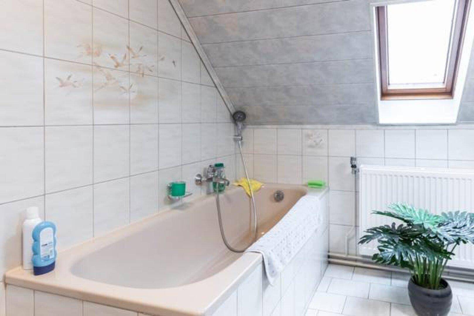 Badezimmer in der Dachgeschosswohnung mit Badewanne, weißen Fliesen und Dachfenster.
