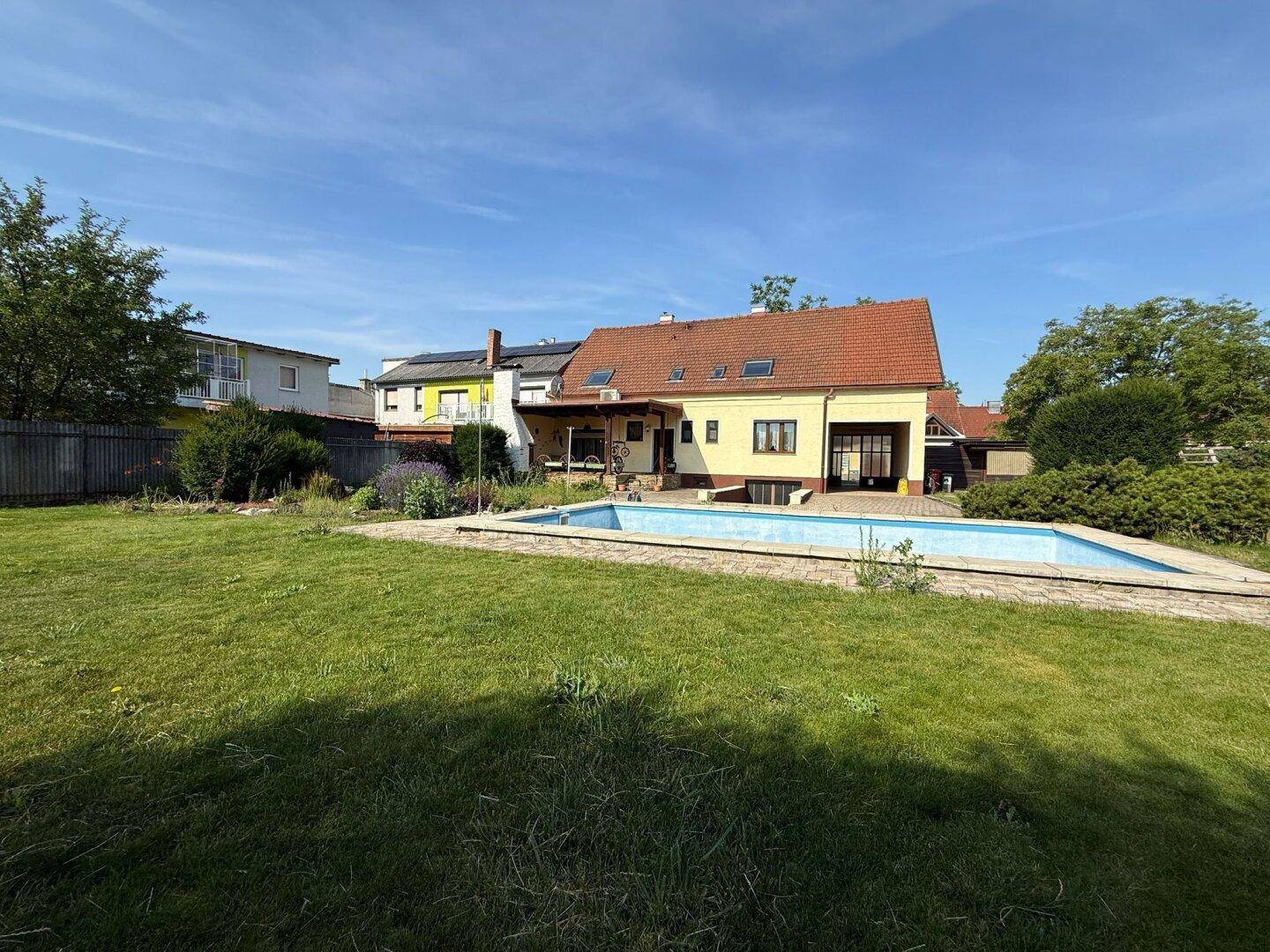 Großer Garten mit Rasenfläche und Swimmingpool hinter dem Einfamilienhaus an einem sonnigen Tag.