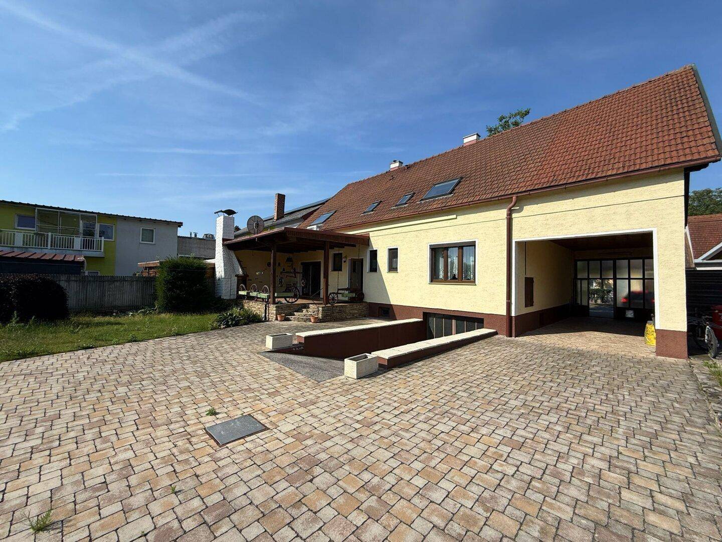 Ansicht des Einfamilienhauses mit gepflasterter Auffahrt und Garagenzugang an einem sonnigen Tag.