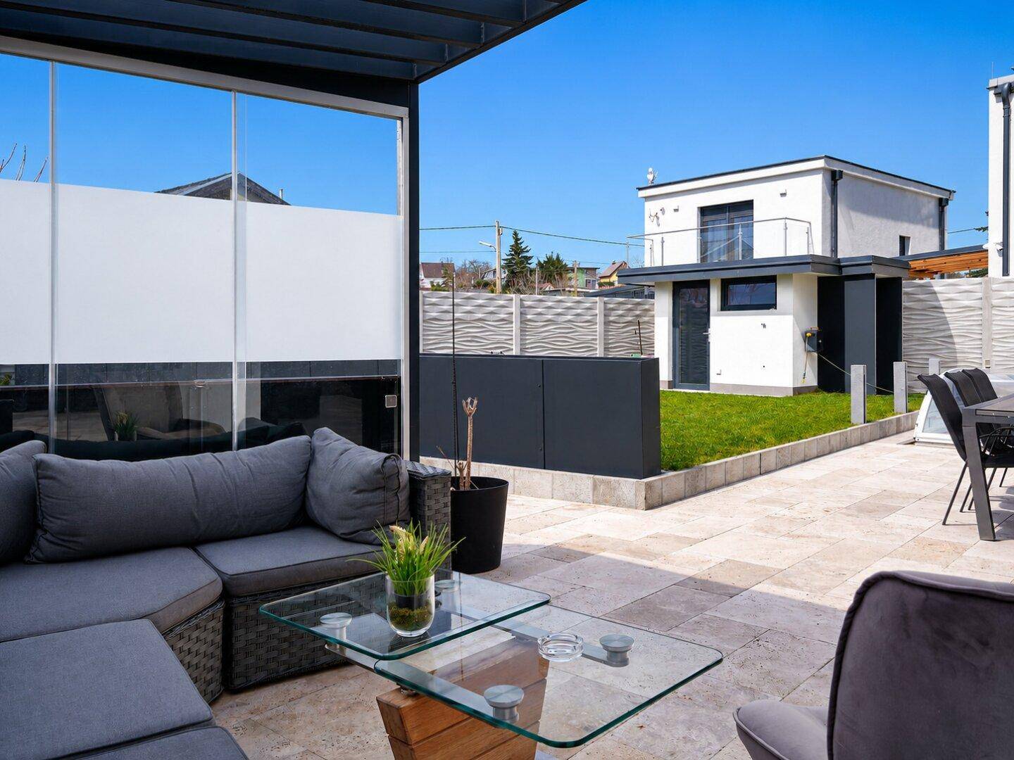 Gemütliche Terrasse mit modernen Loungemöbeln und Blick auf den Garten und ein weiteres Gebäude.