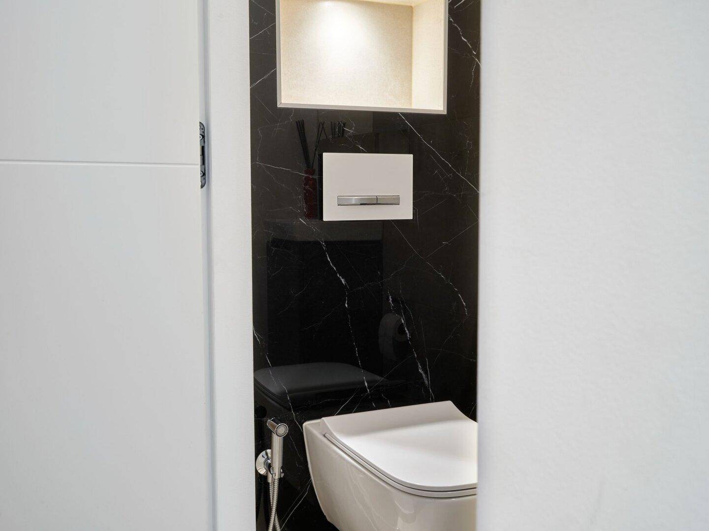 Modernes Gäste-WC mit wandhängender Toilette und schwarzer Marmorwandverkleidung.