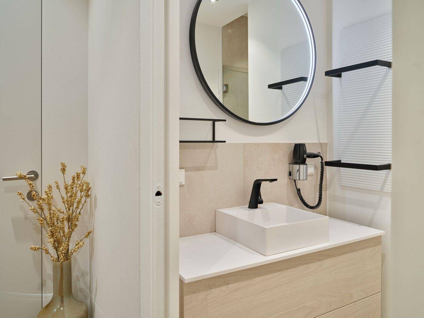 Modernes Badezimmer mit Einzelwaschbecken, rundem Spiegel und beheiztem Handtuchhalter.