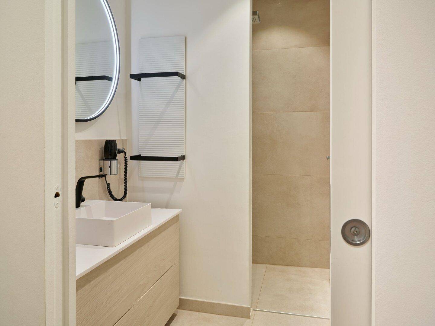 Modernes Badezimmer mit Einzelwaschbecken, rundem Spiegel und begehbarer Dusche.