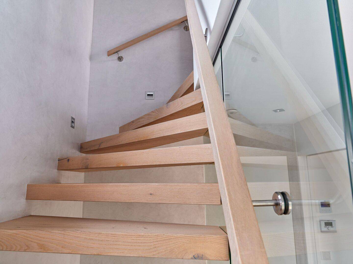 Elegante Holztreppe mit Glasgeländer und minimalistischem Design in einem hellen Treppenhaus.