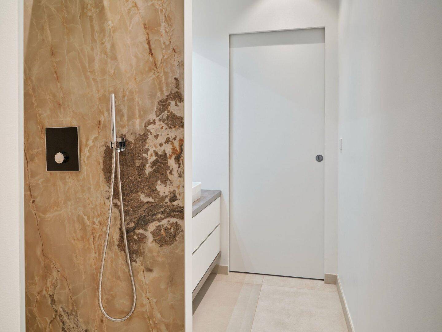 Moderne Dusche mit Handbrause und luxuriöser Marmorwandverkleidung in einem hellen Badezimmer.