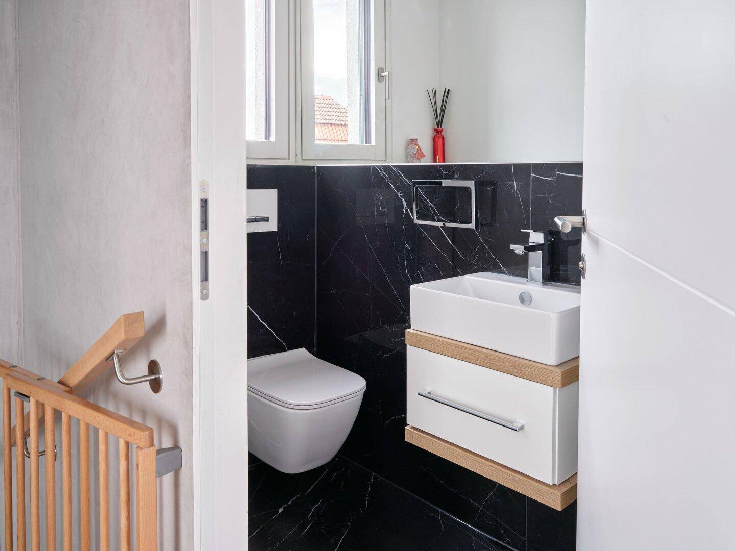 Modernes Gäste-WC mit schwarzem Marmorfliesen, wandhängendem WC und kleinem Waschbecken unter dem Fenster.