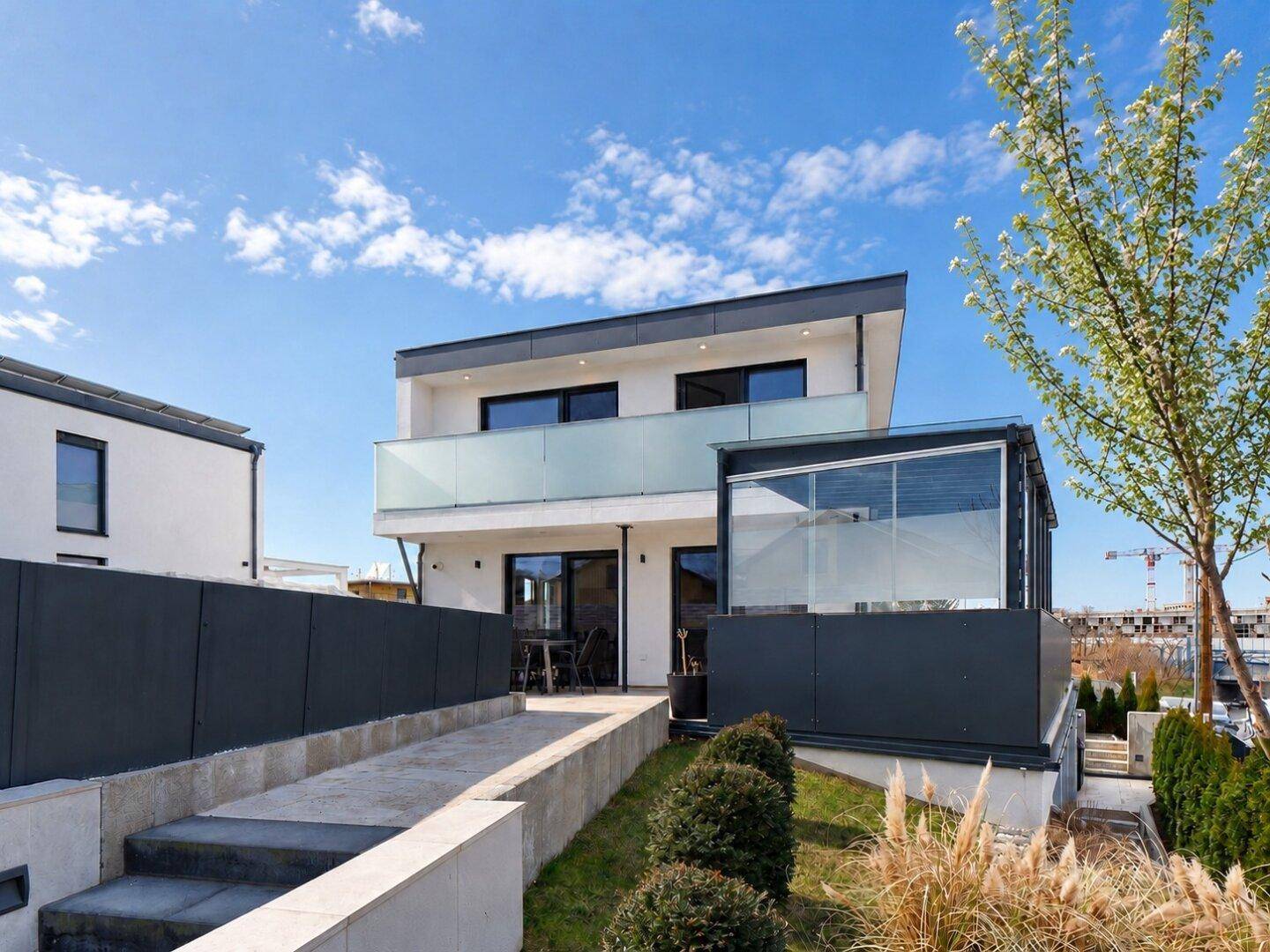 Modernes Haus mit gepflegtem Garten, Terrasse und einem verglasten Anbau unter blauem Himmel.