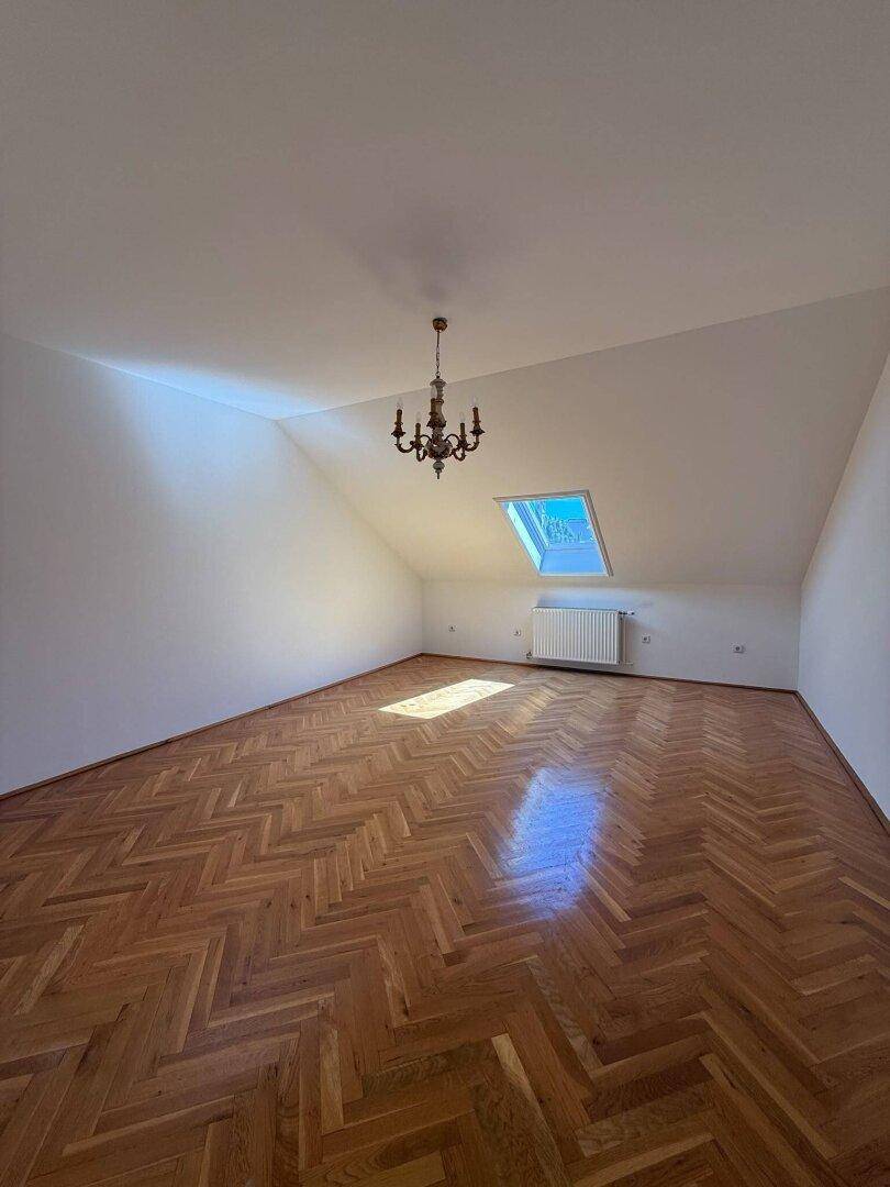 Geräumiges Zimmer im Dachgeschoss mit Fischgrätparkett, Dachfenster und Kronleuchter.