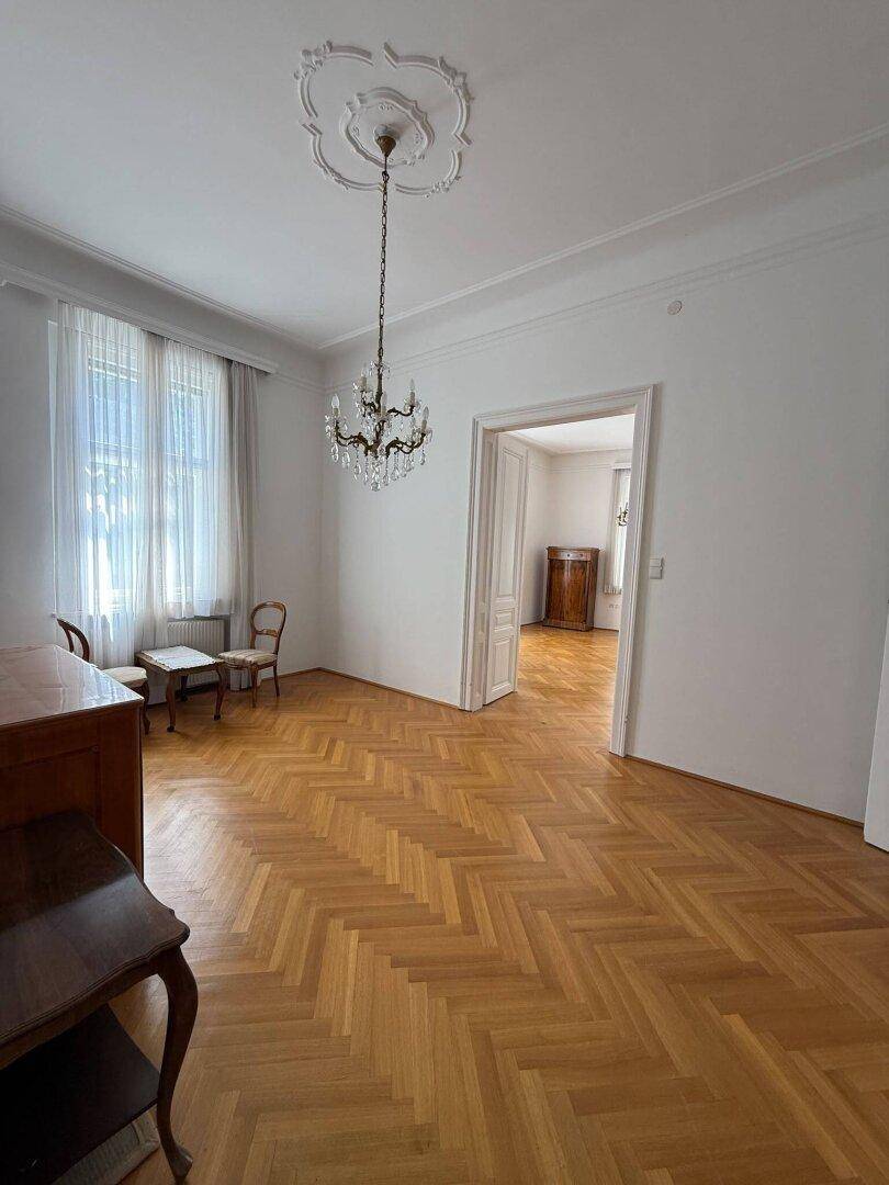 Helles Wohnzimmer mit Fischgrätparkett, Stuckdecke und großem Fenster.