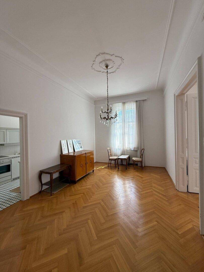 Geräumiges Wohnzimmer mit Fischgrätparkett, Stuckdecke und klassischem Mobiliar.