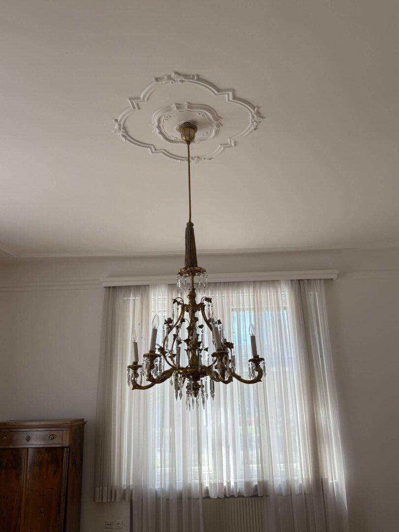 Detailaufnahme eines eleganten Kronleuchters und der verzierten Stuckdecke.