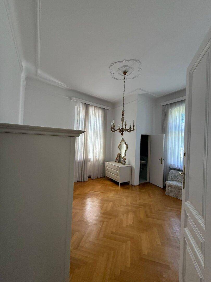 Helles Schlafzimmer mit Fischgrätparkett, Stuckdecke und klassischem Mobiliar.