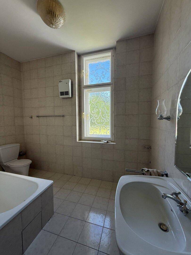 Badezimmer mit beigefarbenen Fliesen, Badewanne, Waschbecken und Fenster.