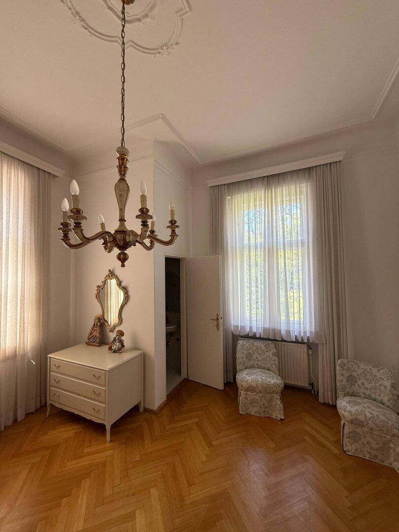 Geräumiges Schlafzimmer mit Fischgrätparkett, Kronleuchter und großen Fenstern.