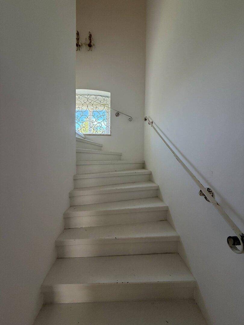 Weiß gestrichene Treppe mit Geländer und einem Fenster mit Buntglas.