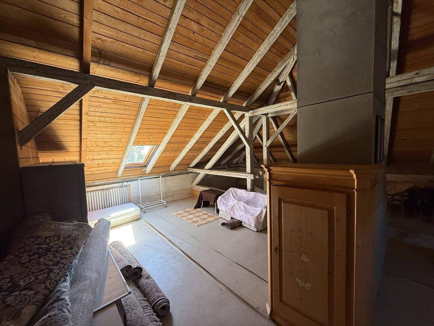 Geräumiger Dachboden mit sichtbaren Holzbalken, Holzverkleidung und einem Dachfenster.