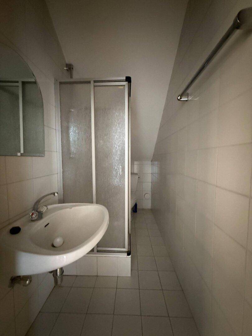 Kleines Badezimmer mit Waschbecken, Duschkabine und schrägen Wänden im Dachgeschoss.