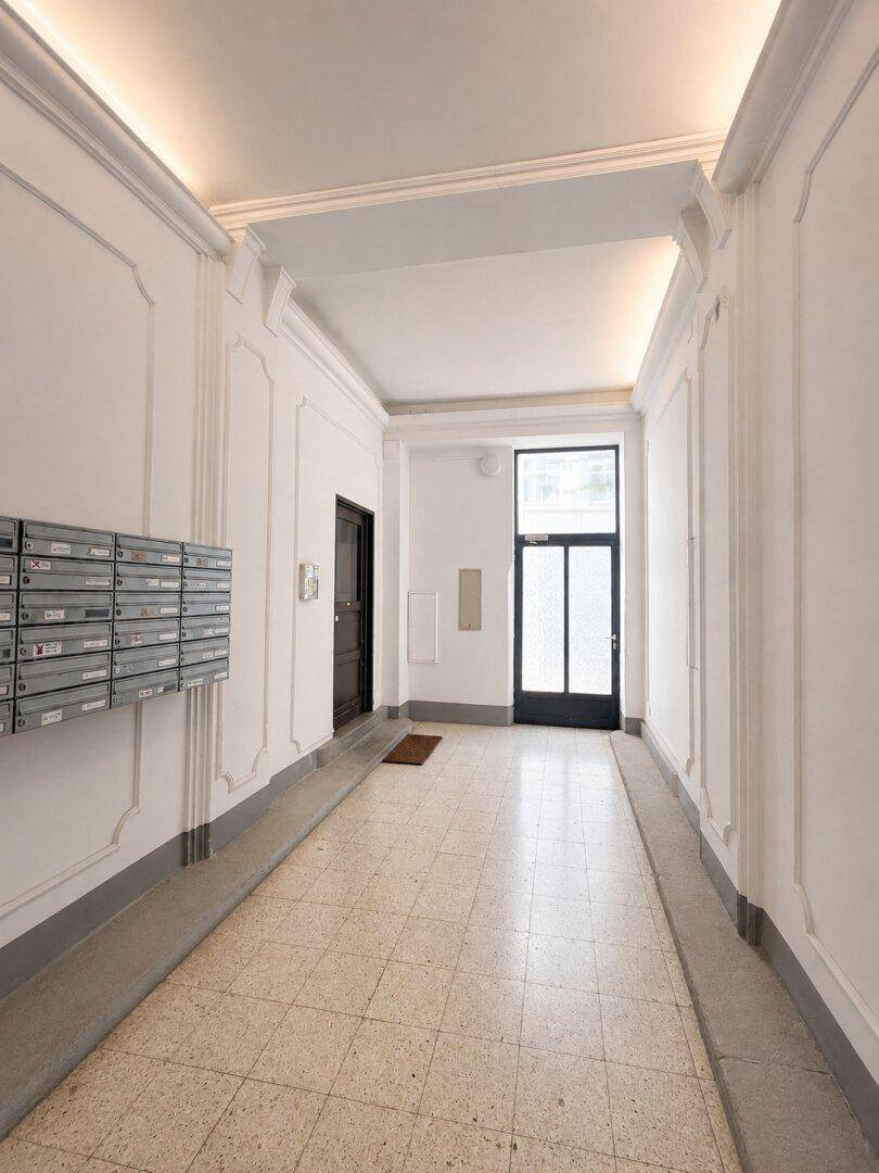 Langer Eingangsbereich mit Briefkästen, hellen Wänden und gemustertem Fliesenboden.