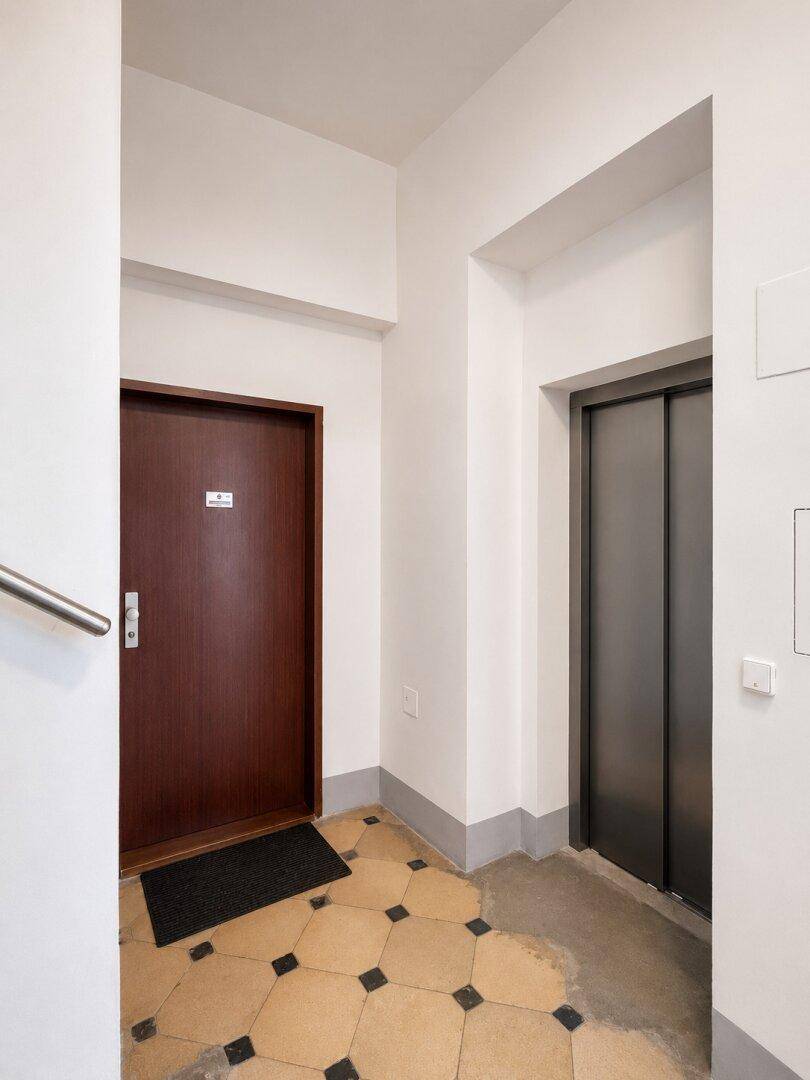 Flur mit Wohnungstür und Aufzug, gekennzeichnet durch einen gemusterten Fliesenboden.